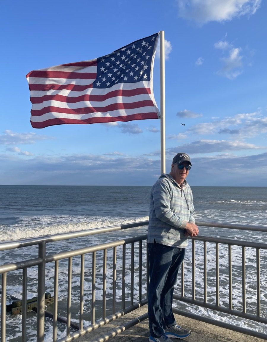 Steve DeVoll standing by the ocean with an American flag in the background